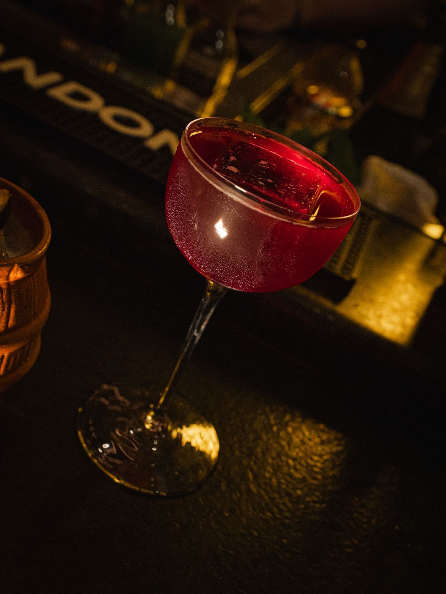 Cóctel rojo con un cubo de hielo en copa, sobre la barra