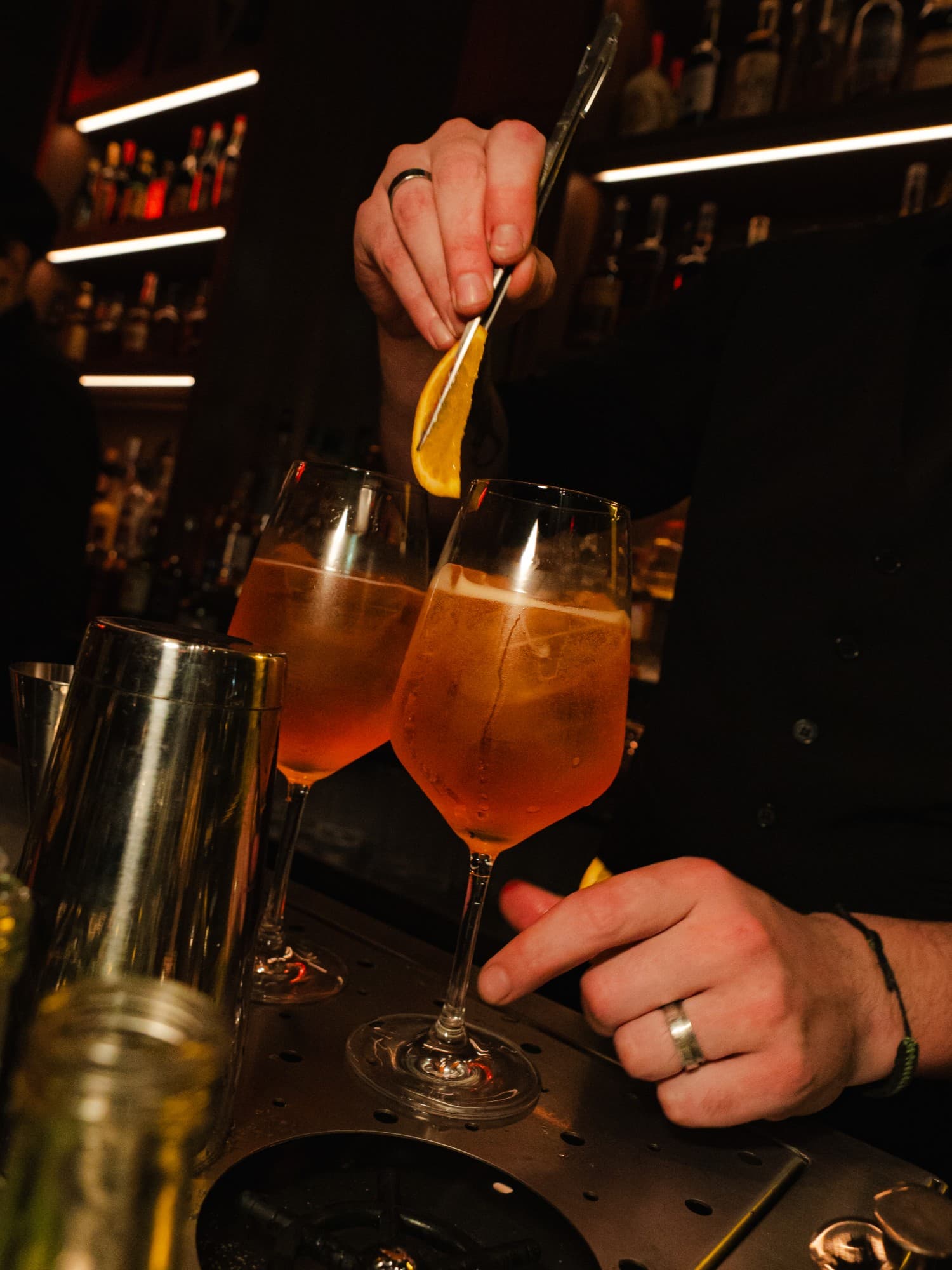Bartender poniéndole con una pinza una rodaja de naranja a dos cócteles en copa
