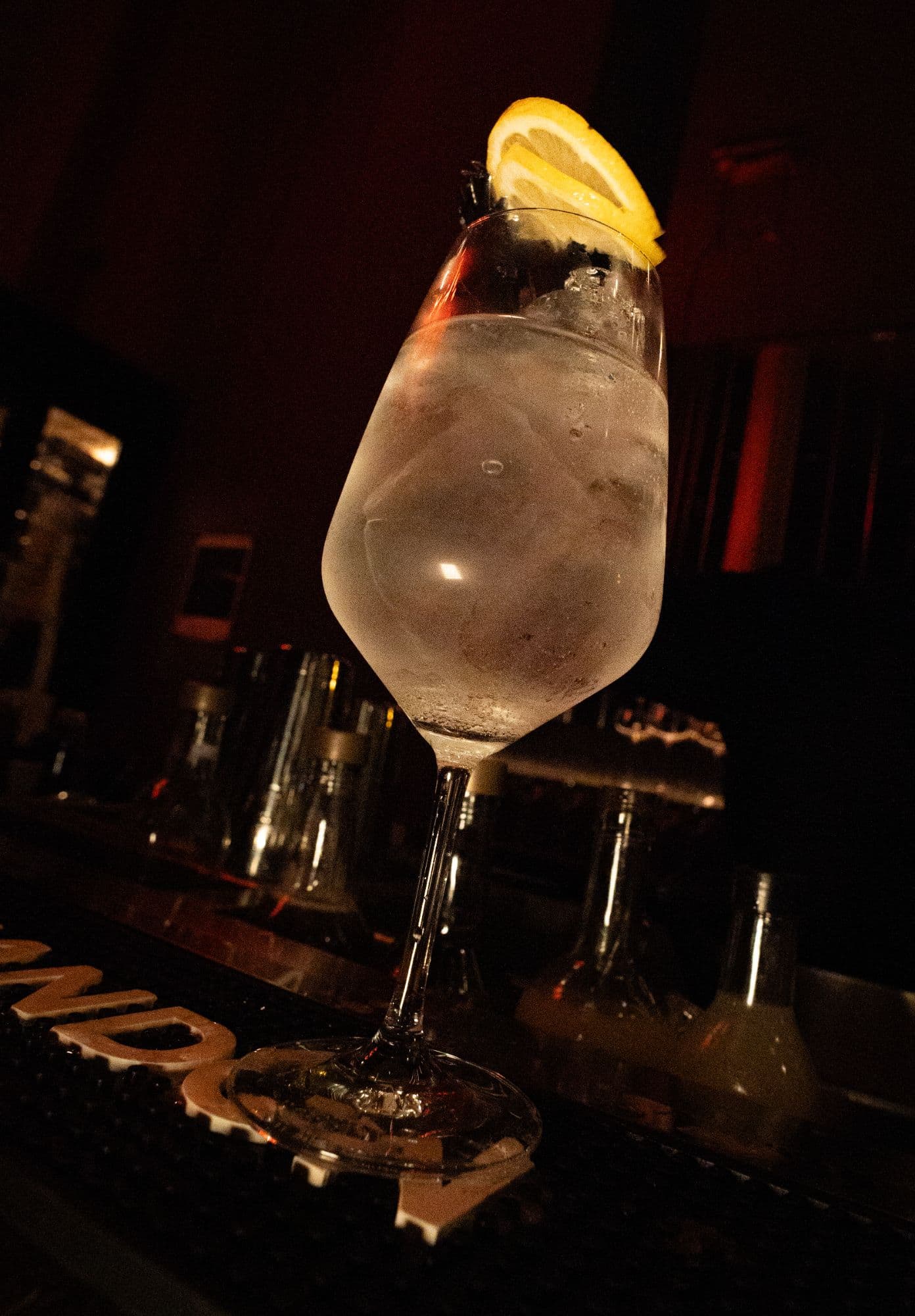 Trago transparente con hielo y una rodaja de limón en copa de vino, sobre la barra